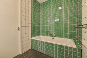 a bathroom with green tiles on the wall and white bathtub in the tub is next to the shower door