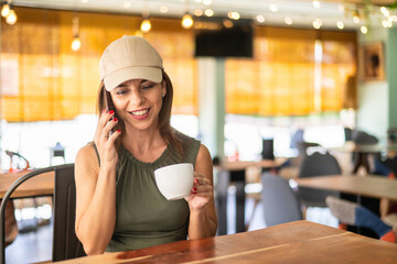 Smiling young adult person having a telephone conversation in a bar. Young beautiful woman using...