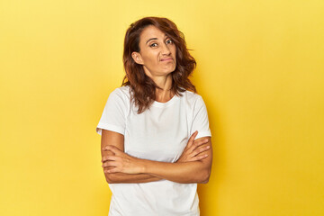 Middle-aged woman on a yellow backdrop unhappy looking in camera with sarcastic expression.