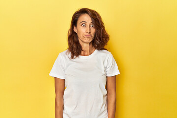 Middle-aged woman on a yellow backdrop sad, serious face, feeling miserable and displeased.