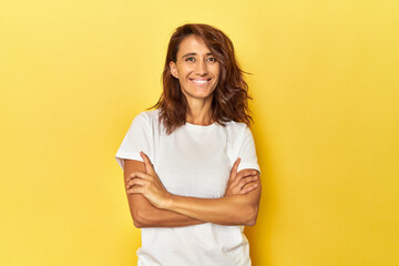 Fototapeta premium Middle-aged woman on a yellow backdrop who feels confident, crossing arms with determination.
