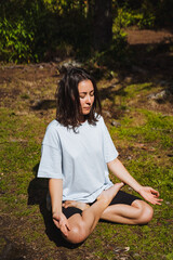 Girl practicing meditation sitting on grass in the forest, deep immersion in yoga practice, summer...