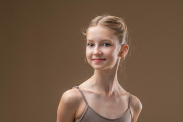 Portrait of a beautiful young girl professional ballerina student with pointe shoes in a leotard on a light beige background.