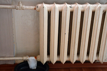 pipes and dusty old cast iron heating radiator with peeling white paint on the wall close-up