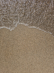 Gentle wave rolling over sand on a beach - 664584393