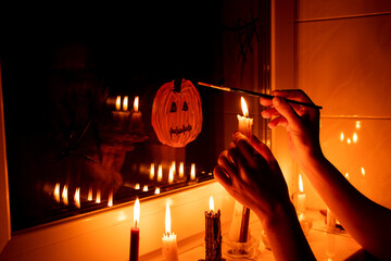 A girl draws a pumpkin for Halloween on the window in an apartment by candlelight