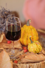 Glass of red wine on wooden table decorated with pumpkins and dried leaves outdoor. Autumn...