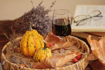 Glass of red wine on wooden table decorated with pumpkins, books and dried leaves outdoor. Autumn composition for Thanksgiving. Autumnal mood