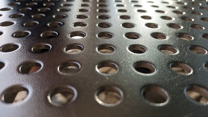 Shiny sheet of metal with holes drilled in it in a row