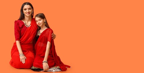 Beautiful Indian woman and her daughter on orange background with space for text