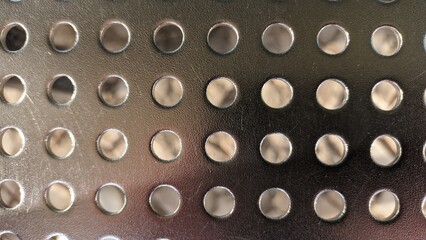 Shiny sheet of metal with holes drilled in it in a row