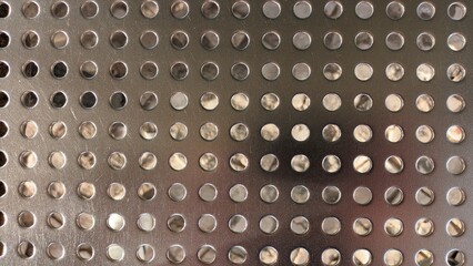 Shiny sheet of metal with holes drilled in it in a row
