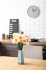 Vase with blooming narcissus flowers on table in modern kitchen