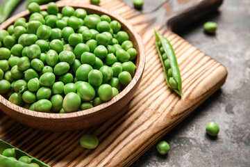 Bowl and wooden board with fresh green peas on black background