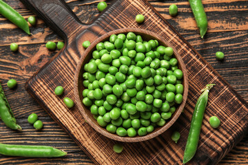 Bowl and board with fresh green peas on wooden background