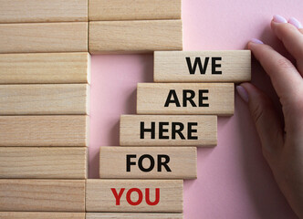 Help symbol. Wooden blocks with words We are here for you. Beautiful pink background. Businessman hand. Business and We are here for you concept. Copy space.