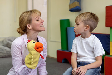 Little boy and speech therapist using colorful toys on session. Psychologist during play therapy with preschooler. Mom and child learn pronouncing sounds. Boy performs articulation exercises for mouth