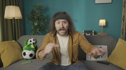 Footage shows a bearded middle-aged man sitting on a couch in an apartment. He looks at the camera, blows his whistle and pulls out a yellow card then a red card. Holds it out to the camera HDR BT2020