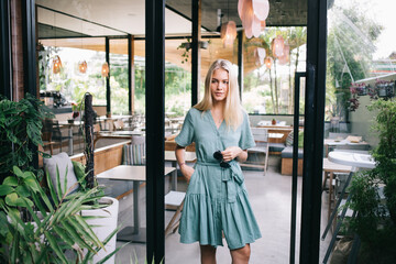 Contemplative hipster girl with trendy sunglasses in hand thinking about leisure pastime in cafe interior, casual dressed woman thoughtful looking away and feeling pondering in local coffee shop