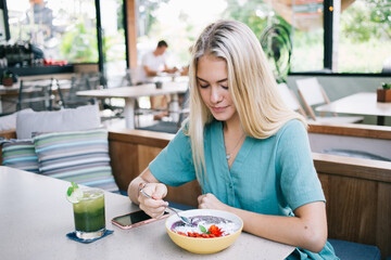Caucasian female ordered bowl with fresh delicious meal during lunch time in local cafe interior with organic food, woman eating vegan delicious meal for breakfast enjoying detox nutrition