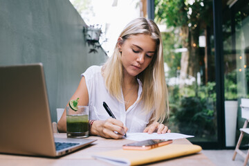 Intelligent woman doing business planning during remote working in street cafeteria, millennial...