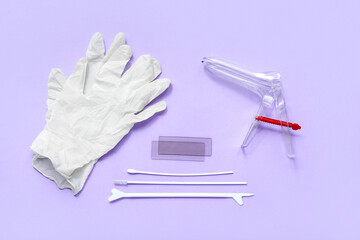 Medical gloves with gynecological speculum and pap smear test tools on lilac background