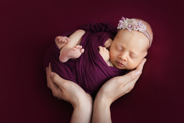newborn girl wrapped in a diaper in a cocoon in the hands of her mother on a pink background. love for children