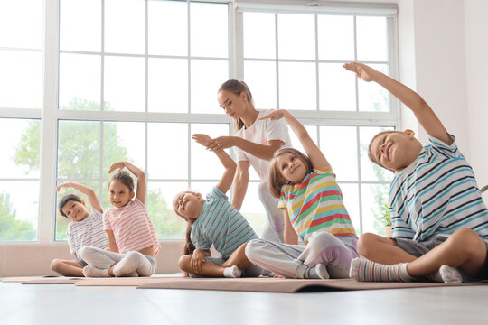 Group of little children practicing yoga with instructor in gym