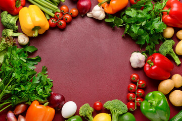 Frame made of fresh vegetables, fruits and greenery on burgundy background