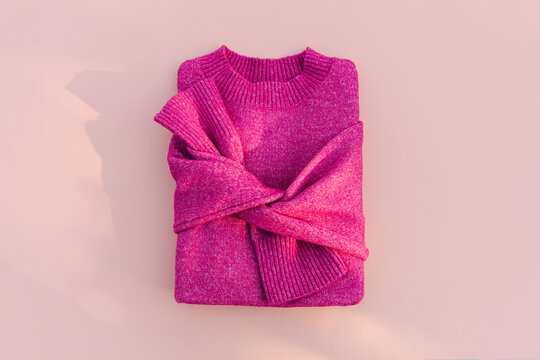 Magenta sweater on pale pink background. Women's jumper stylish autumn or winter clothes. Fashion outfit in fuchsia color. Cozy bright  fall look. Flat lay, top view.