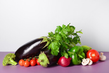 Fresh vegetables and greenery on purple table near white wall