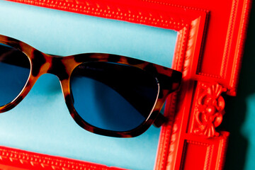 Black sunglasses on red art frame and blue background close up