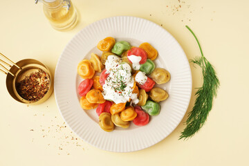 Plate of boiled colorful dumplings with sour cream and dill on yellow background