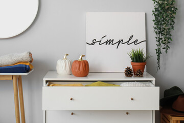 Chest of drawers with clean clothes and autumn decor in room