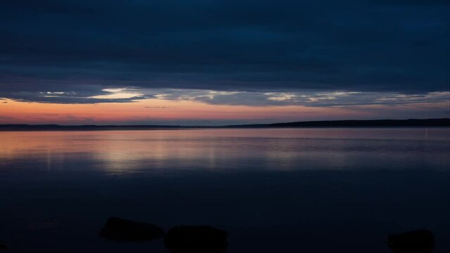 Time lapse of cloud movement over a lake in Finland in evening with forests in the horizon and rocks in the foreground