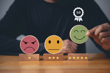 Hand choosing a smiley face on a wooden block circle to rate the best business services and...