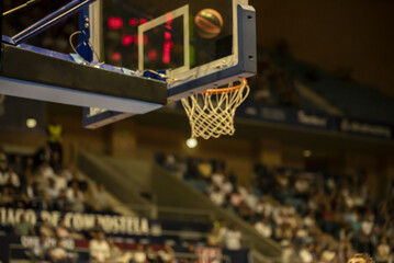 blurred image of a basketball approaching the hoop in the air in the foreground the basket and the...