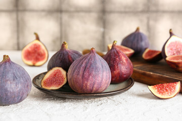 Plate and wooden board with fresh ripe figs on white table