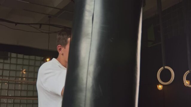 Caucasian man boxing trainer beating big punching bag in modern gym. Fitness coach warm up before hard exercises