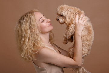 a girl holds a cute Maltipoo dog in her arms close-up on a plain beige background, the concept of love for a dog
