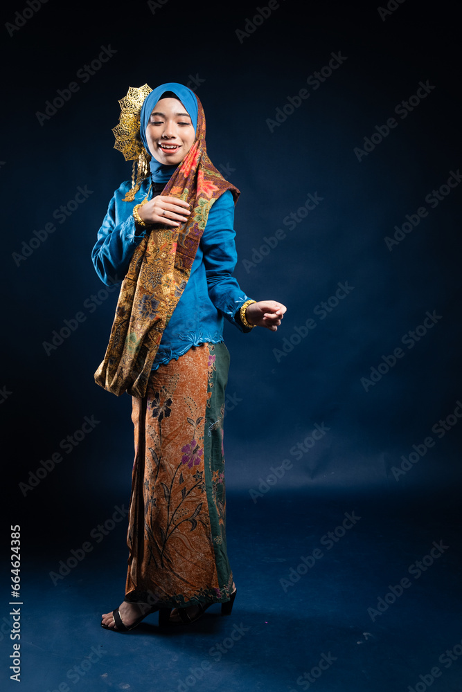 Wall mural Muslim woman wearing traditional wear blue kebaya and hijab isolated on blue background. Idul Fitri and hijab fashion concept.