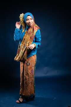 Muslim woman wearing traditional wear blue kebaya and hijab isolated on blue background. Idul Fitri and hijab fashion concept.