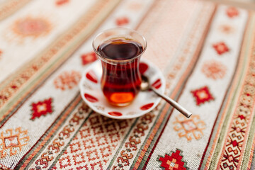 Turkish black tea in national dishes stands on the table with a napkin with Turkish patterns....