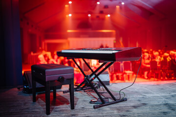 electronic keyboard set up on a stage with a stool beside it, ready for a performance. The stage is...