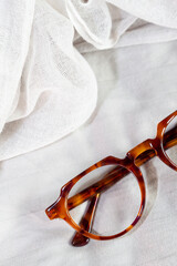 Pair of glasses with tortoise frame on white linen background top view