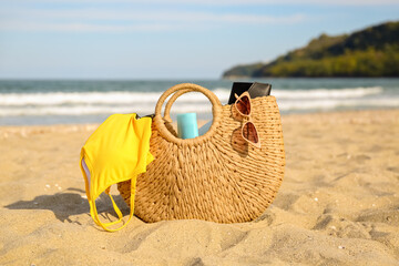 Straw bag with bottle of sunscreen cream and swimsuit on sand