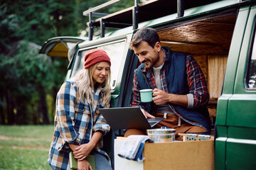 Happy couple using laptop while relaxing in camper trailer in woods.