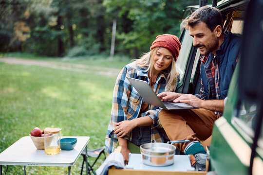 Happy couple of campers surfing the net of on laptop while relaxing in their van in nature.