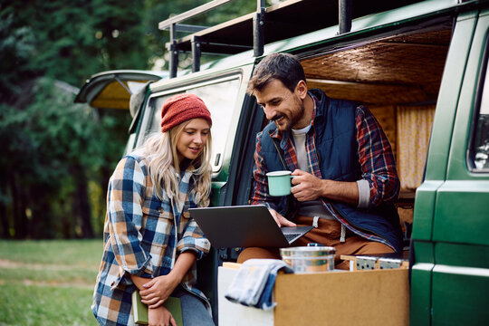Happy couple using laptop while relaxing in camper trailer in woods. - Powered by Adobe