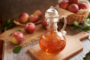 A jug of apple cider vinegar with fresh apples on a table